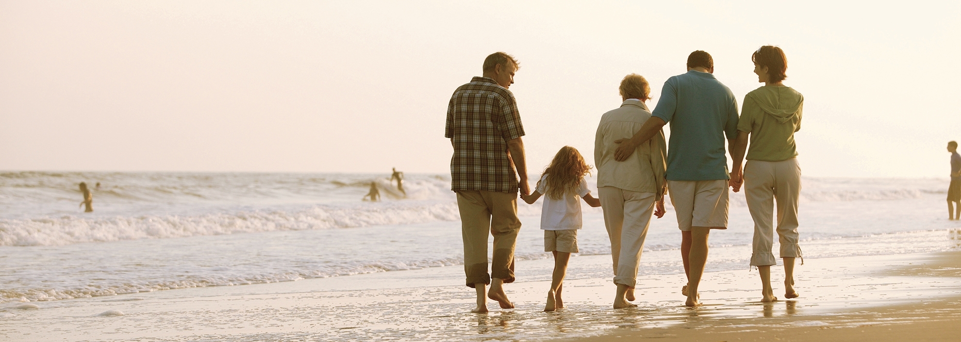 Multiple Generational Family walking on sunny beach at dusk 